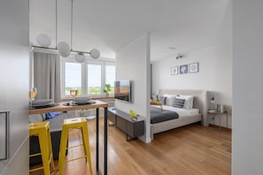 A modern apartment with a kitchen, dining area, and a bedroom with a bed, bedside table, and a TV. - Lumina apart near the Visla embankment (Warsaw)
