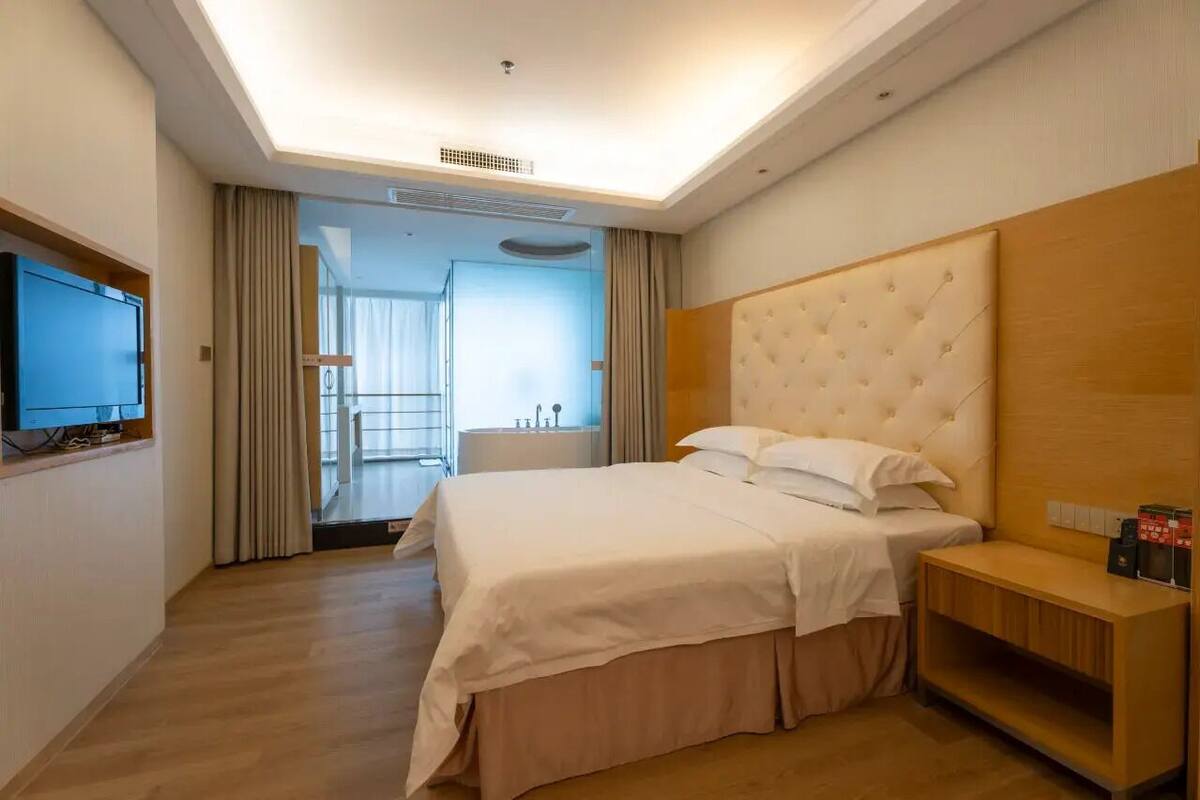 Habitación de hotel con una cama grande, un televisor, una mesita de noche de madera y vistas al exterior.