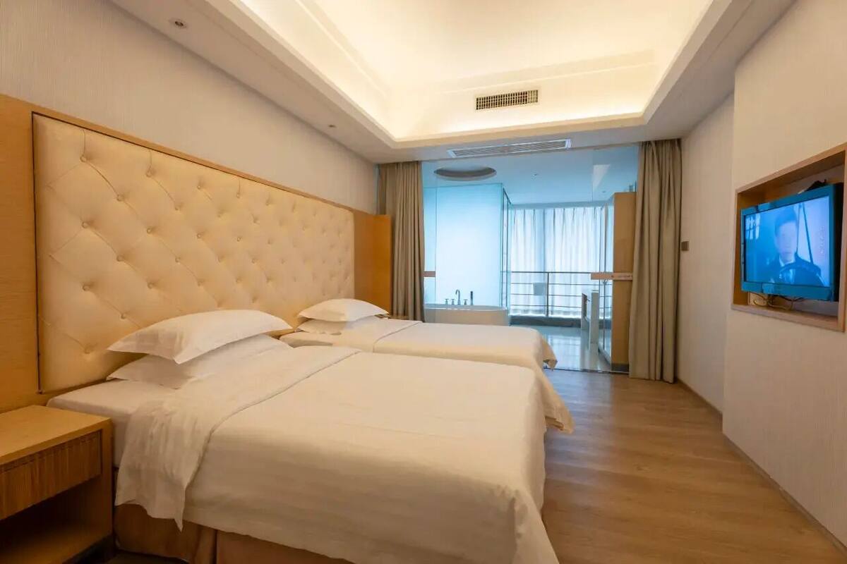 Habitación de hotel con dos camas, un televisor y vistas al exterior.