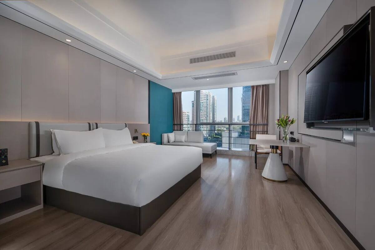 Habitación de hotel moderna con una cama grande, televisor, escritorio y vistas a la ciudad.