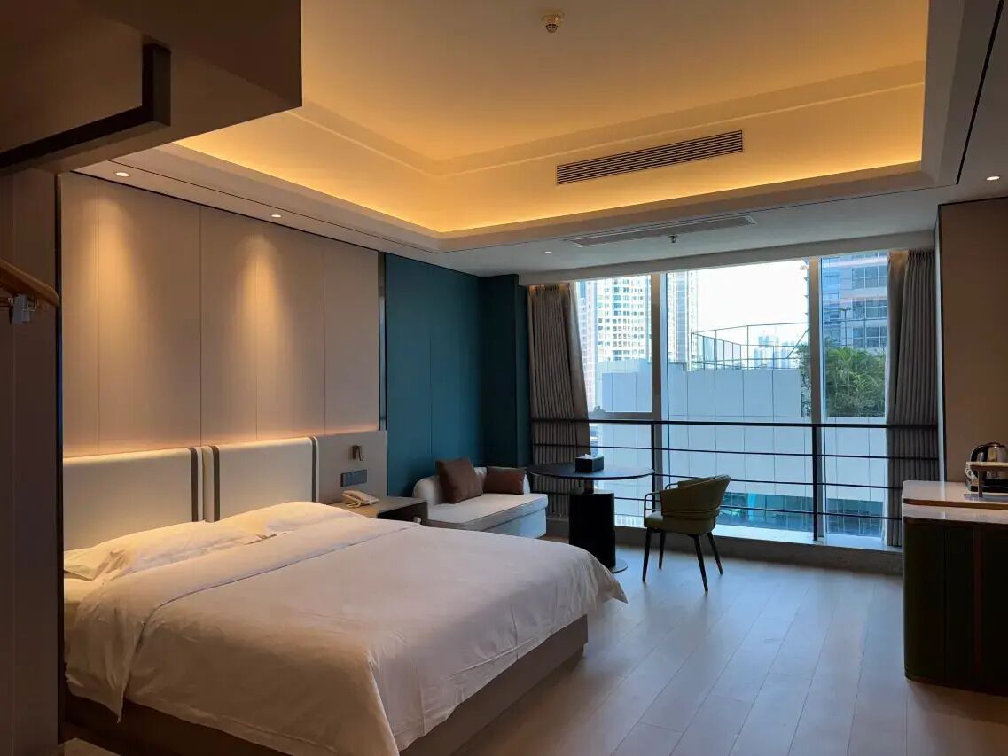 A modern hotel room with a large bed, a desk, a chair, and a view of the city.