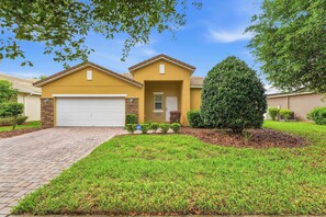 A residential house with a garage, a well-maintained lawn, and a large tree. - Wishes Villa Pool & Hot Tub (Kissimmee)
