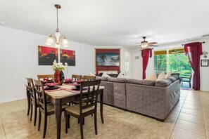 A dining area with a wooden table and chairs, a sofa, and a ceiling fan. - Wishes Villa Pool & Hot Tub (Kissimmee)