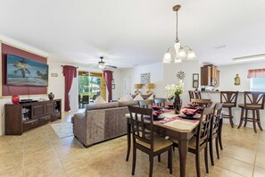 A dining area with a table set for four, a sofa, a TV, and a ceiling fan. - Wishes Villa Pool & Hot Tub (Kissimmee)