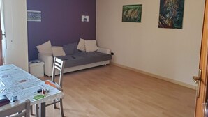 Una habitación con una cama, una mesa con mantel, una silla y dos cuadros en la pared.