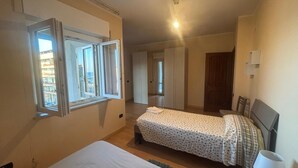 Un dormitorio con cama, ventana, mesita de noche y puerta que da a otra habitación.