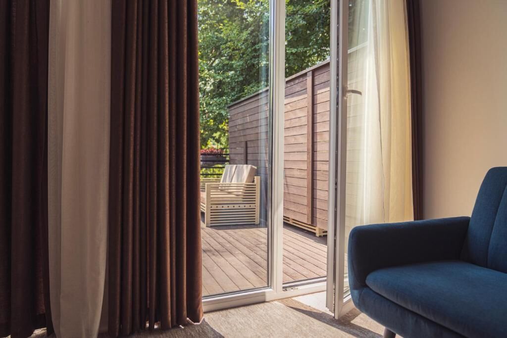 A room with a sliding glass door leading to an outdoor deck, a blue sofa, and a wooden deck with a bench.
