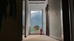 A hallway with a carpeted floor, a white door at the end, and a window with a view of greenery.