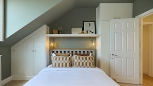 A bedroom with a bed, checkered pillows, a shelf with framed pictures, and a door. - The Eaves on Santos Road (London)