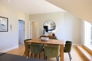 A dining area with a wooden table, green chairs, a bowl, and a mirror on the wall. - The Eaves on Santos Road (London)