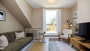 A living room with a sofa, a coffee table, a TV, and a window. - The Eaves on Santos Road (London)