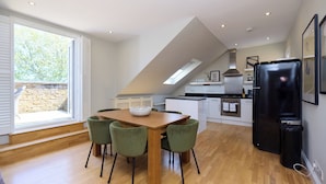 A modern kitchen with a dining area, wooden flooring, and a skylight. - The Eaves on Santos Road (London)