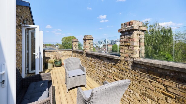 A balcony with wicker furniture, stone walls, and a view of the cityscape. - The Eaves on Santos Road (London)