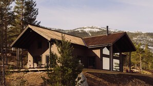Une cabane dotée d’une grande terrasse, d’un porche abrité et offrant une vue sur des montagnes enneigées.