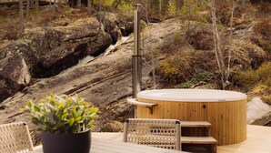 Un bain à remous doté d’une terrasse en bois, entouré d’un paysage rocheux et d’arbres.