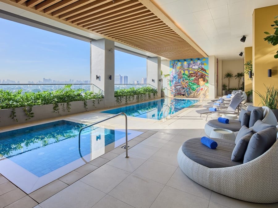 Una piscina en la azotea con vistas despejadas al horizonte de la ciudad, un mural y asientos de descanso.