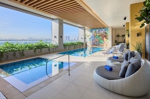 A rooftop pool with clear views of the city skyline, a mural, and lounge seating.