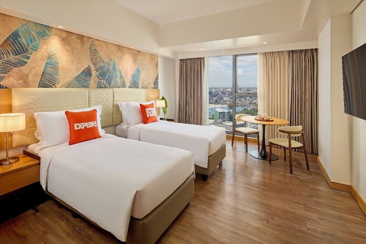 Habitació d'hotel amb dos llits, vistes a la ciutat, una taula de dinar i una gran obra d'art abstracta a la paret.