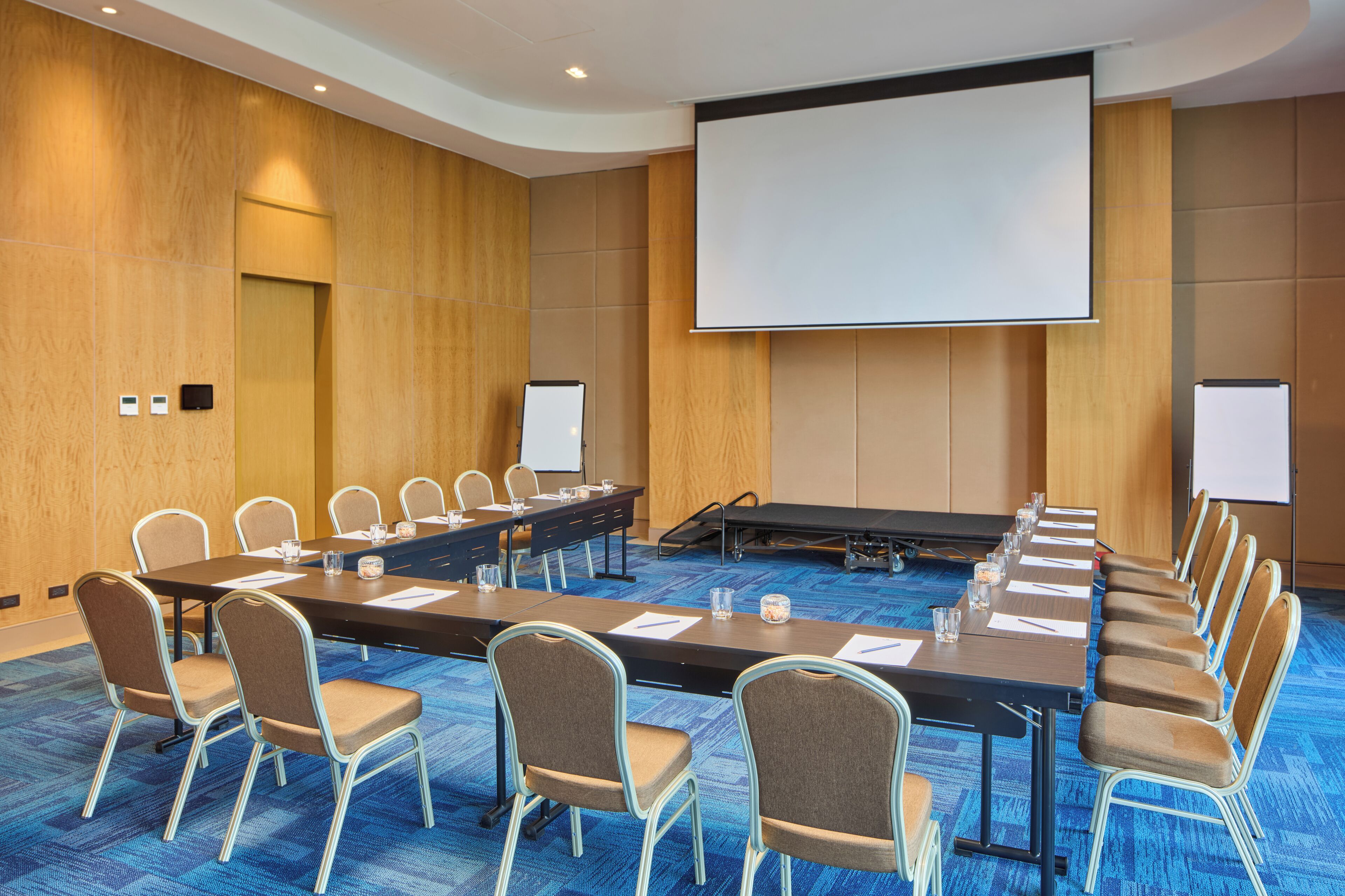 A conference room with a long table, chairs, a projector screen, and a whiteboard.
