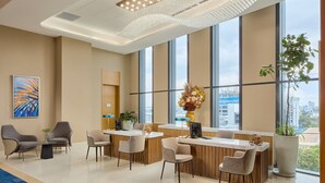 A modern hotel lobby with a reception desk, seating area, large windows, and a decorative chandelier. - Alino Hotel (Quezon City)