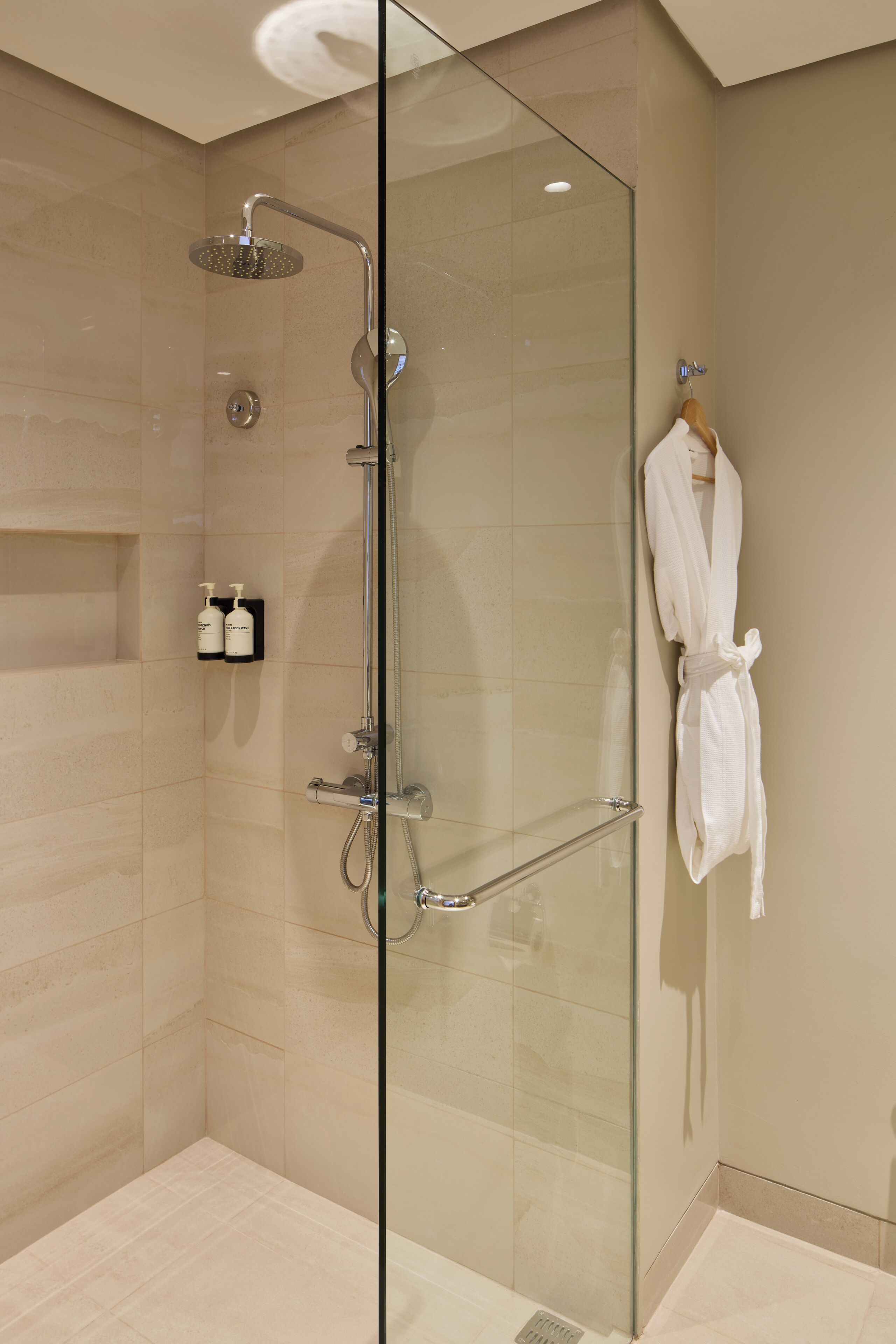 Ducha envuelta en vidrio con tres duchas: una manual, una de mano y una de pared.