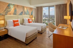 A hotel room with two beds, a desk, a chair, a large window with a city view, and a decorative wall.