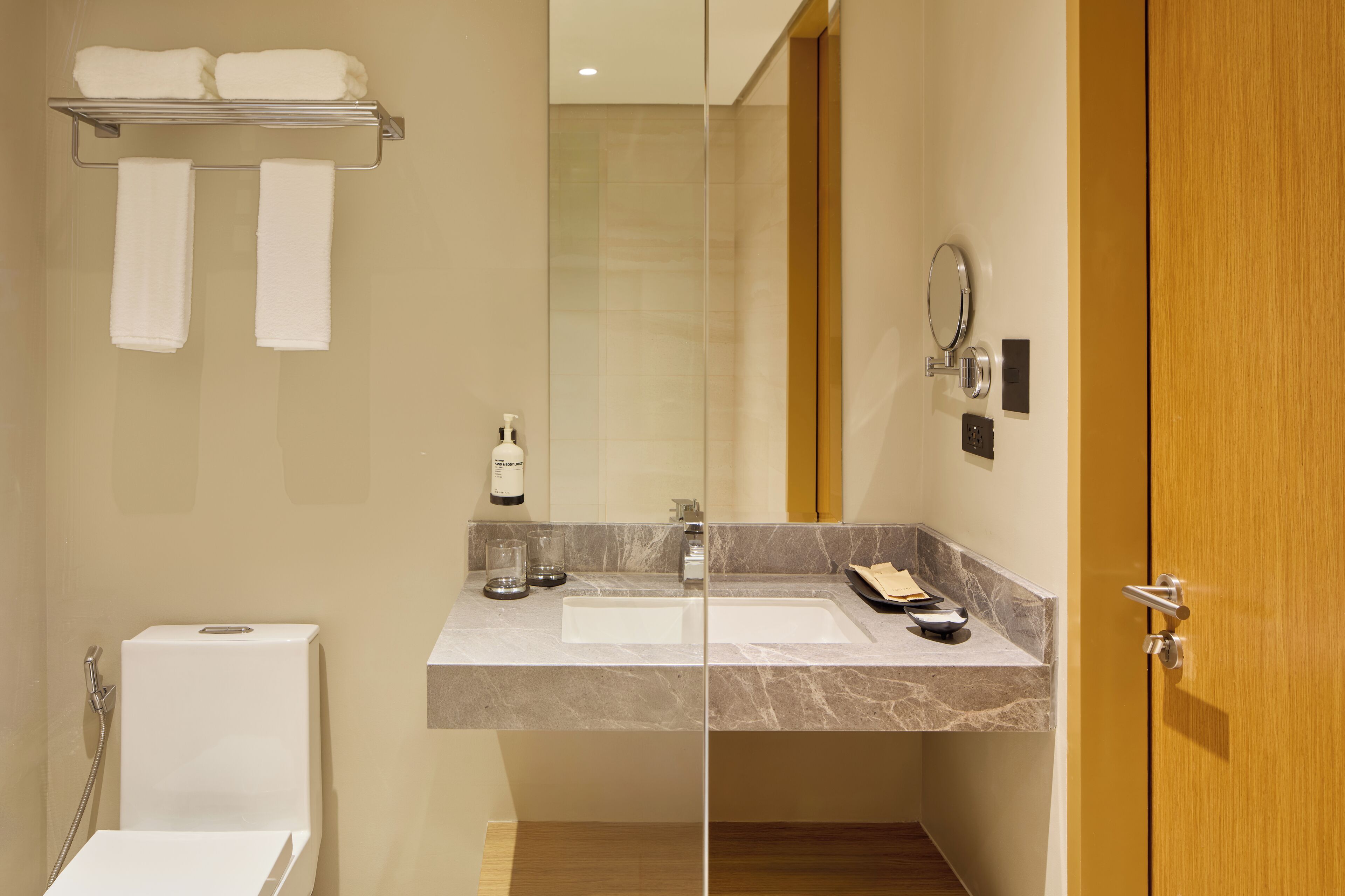 A modern bathroom with a glass shower enclosure, a white toilet, a vanity with a marble countertop, and a wooden door.
