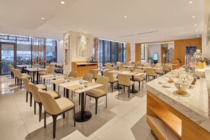 A modern dining area with multiple tables and chairs, a bar area, and large windows offering views.