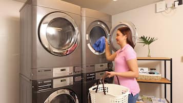 A laundry room with stacked washers and dryers, a basket, and a shelf with magazines.