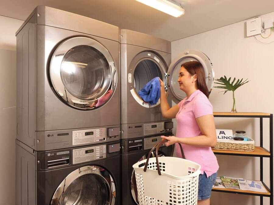 A laundry room with stacked washers and dryers, a basket, and a shelf with magazines.