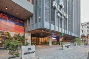 Entrada de hotel con fachada moderna, un gran letrero del Hotel Alino y un cielo despejado.
