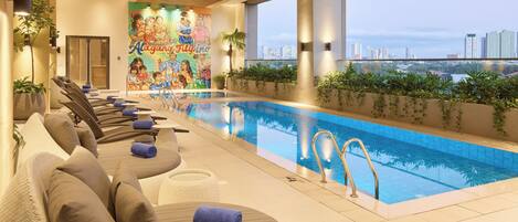 Un área de piscina interior moderna con sillones de descanso y un mural en la pared.