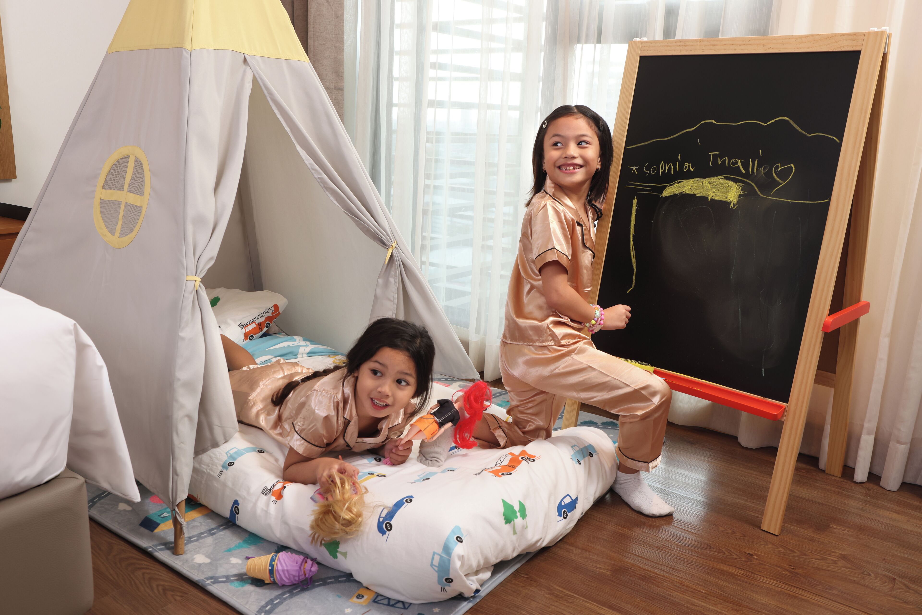 Two children in a play tent and a blackboard with chalk drawings.