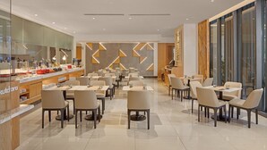 A modern dining area with tables and chairs, a kitchen area, and a large window providing a view. - Alino Hotel (Quezon City)