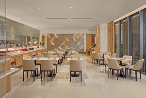 A modern dining area with tables and chairs, a kitchen area, and a large window providing a view.
