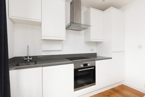 A modern kitchen with white cabinets, a stainless steel range hood, a built-in oven, and a black countertop.