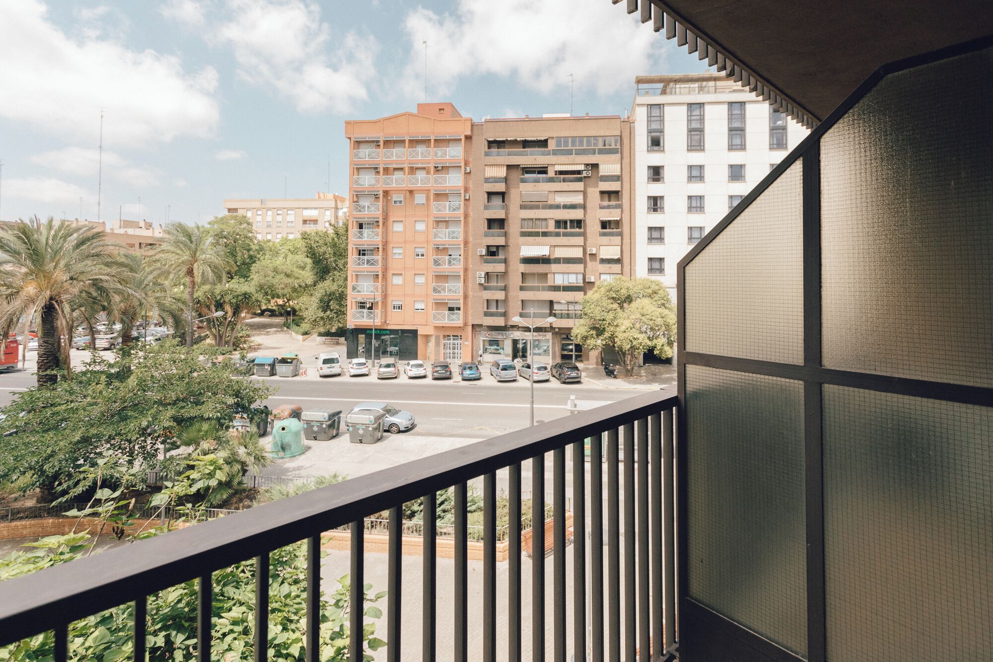 Uma varanda com vista para um prédio de vários andares, carros estacionados e vegetação.