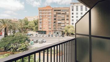 Uma varanda com vista para um prédio de vários andares, carros estacionados e vegetação.
