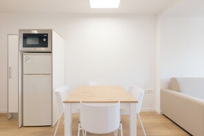A compact kitchen with a microwave, refrigerator, and a wooden dining table with white chairs. - Monlar Campanar (Valencia)