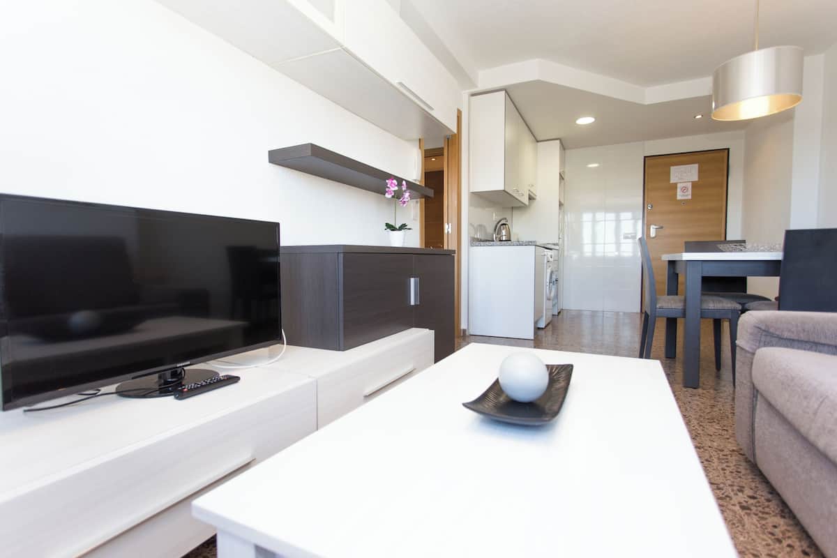 A modern living room with a flat-screen TV, a coffee table with a decorative sphere, a sofa, and a dining area with a table and chairs.