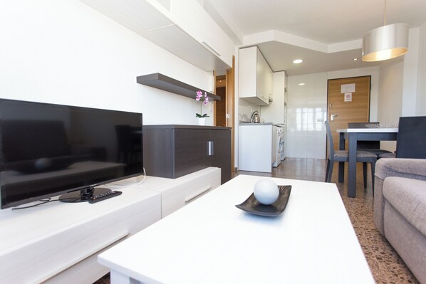 A modern living room with a flat-screen TV, a coffee table with a decorative sphere, a sofa, and a dining area with a table and chairs. - Monlar Campanar (Valencia)