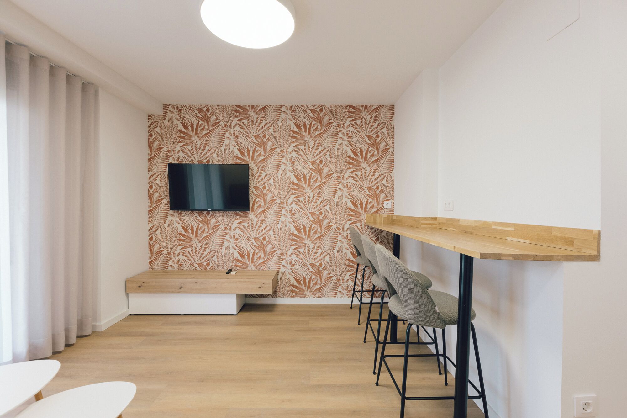 A modern room with a flat-screen TV mounted on a patterned wall, a wooden bench, and a bar area with stools.