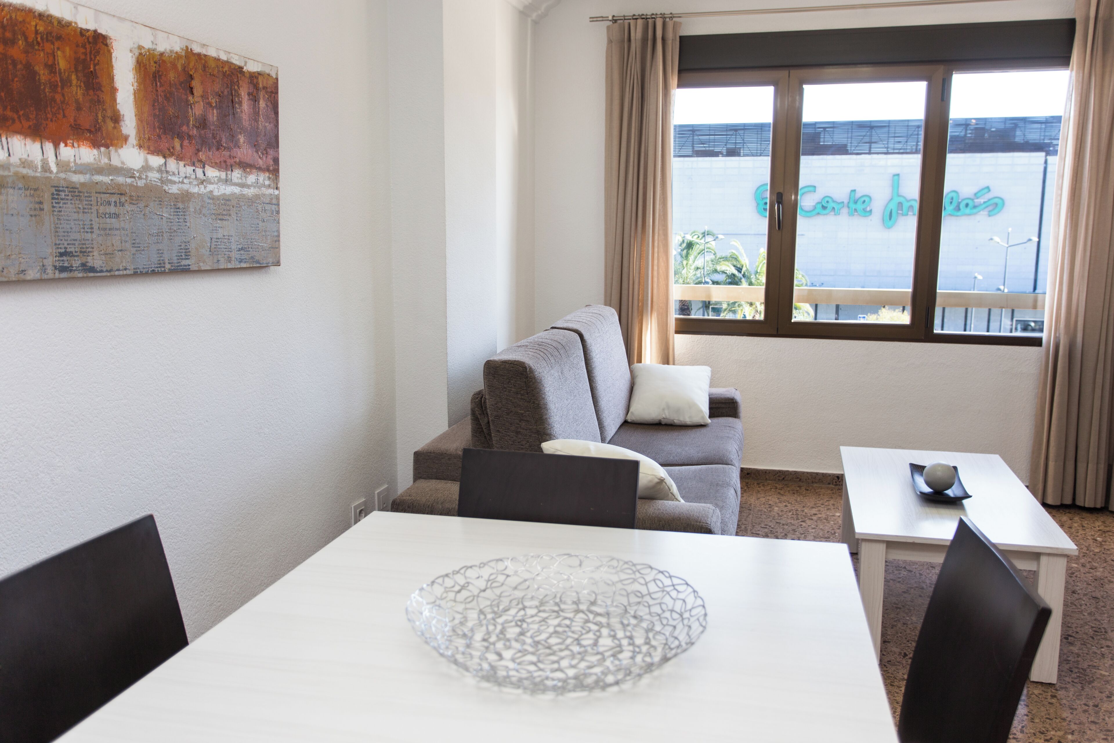 Quarto com sofá, mesa de jantar e uma grande janela com vista para um edifício.