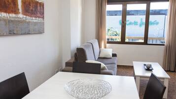 Quarto com sofá, mesa de jantar e uma grande janela com vista para um edifício.