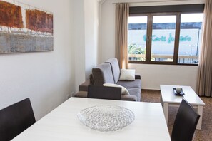 Quarto com sofá, mesa de jantar e uma grande janela com vista para um edifício.
