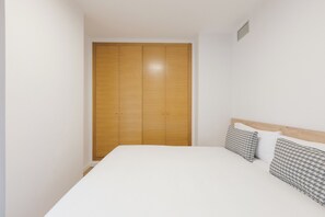 A bedroom with a wooden wardrobe, a bed with white bedding, and patterned pillows. - Monlar Campanar (Valencia)