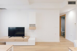 A modern living room with a flat-screen TV on a wooden table, a built-in shelf with glassware, and a visible bathroom door. - Monlar Campanar (Valencia)