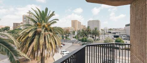 A balcony with a view of a cityscape, palm trees, and a parking lot.