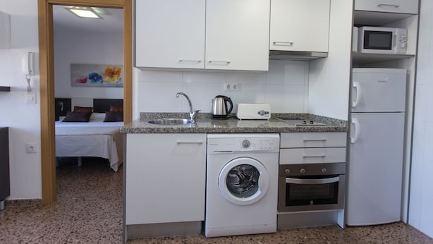 A compact kitchen with a washing machine, oven, microwave, and a small refrigerator. - Monlar Campanar (Valencia)