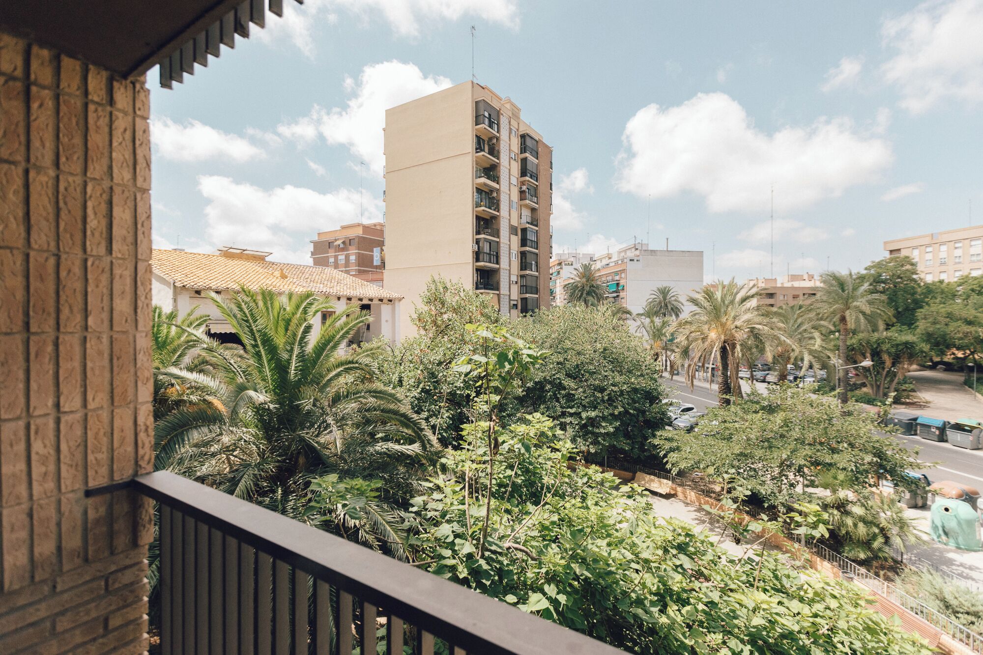 Un balcón con vistas a un edificio alto, palmeras y una carretera.